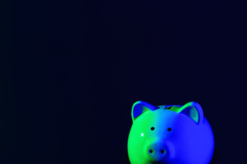 Piggy bank on a dark background with green-blue backlight, copy space. Banking concept. Bright neon lights on a black background