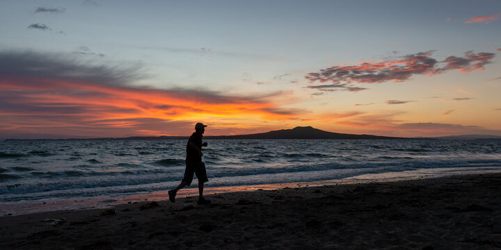 Silhouette image of man running on Milford beach at sunrise, Rangitoto Island in the background, Auckland.