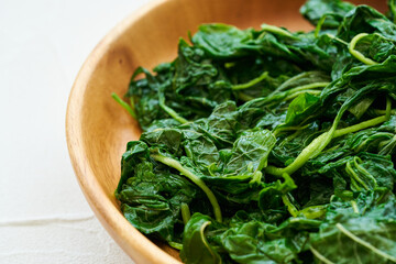 close up green cook leaf spinach salad in wood bowl on white table background. leaves spinach or...