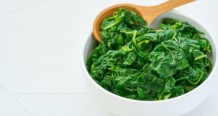 close up green cook leaf spinach salad in white bowl on white table background. leaves spinach or heap of spinach food salad                                                                      
