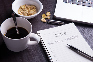 Conceptual,Top view office desk mockup: laptop, notebook, smartphone, snack bean, and cup of coffee on rustic brown wooden desk. New year 2023 resolution