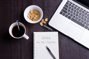 Conceptual,Top view office desk mockup: laptop, notebook, smartphone, snack bean, and cup of coffee on rustic brown wooden desk. New year 2023 resolution