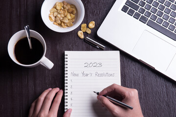 Conceptual,Top view office desk mockup: laptop, notebook, smartphone, snack bean, and cup of coffee on rustic brown wooden desk with hand writing. New year 2023 resolution