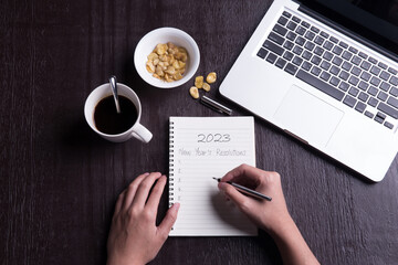 Conceptual,Top view office desk mockup: laptop, notebook, smartphone, snack bean, and cup of coffee on rustic brown wooden desk with hand writing. New year 2023 resolution