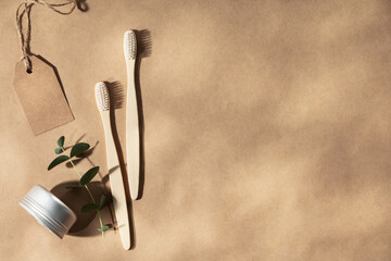 Two natural wooden toothbrushes on natural beige background with leaves shadows, flat lay, top view
