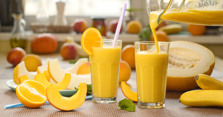 Melon banana orange Smoothie is poured into a glass on the background of fresh fruits