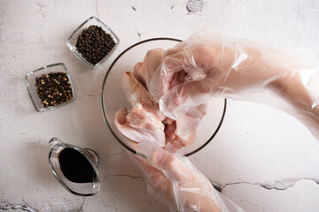 Gloved hands stir the wings with soy baking sauce. A dish of Asian cuisine.