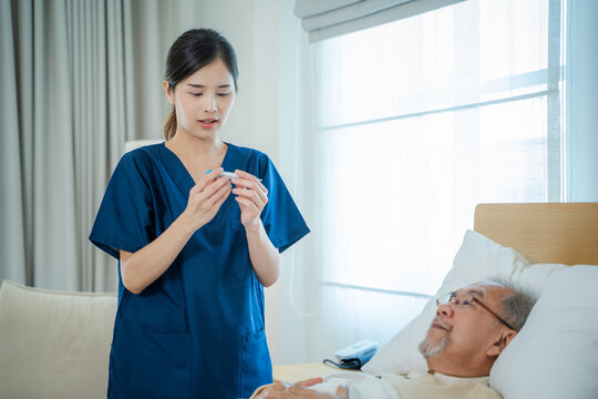 Nurse Holding Digital Thermometer And Senior Man In Bedroom In House.