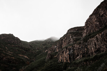 Rocky texture of the mountains of Laurissilva Forest covered in fog and a white pale sky in Madeira island, Portugal. Landscape background in moody tones and empty space for text