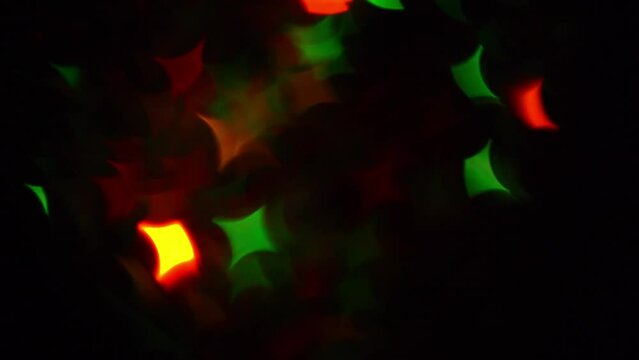 Twinkling Christmas Stars Bokeh Diagonal Overflow. Abstract festive moving background. Red and green quadrangular bokeh stars on a dark background can be used as a transition or overlay.