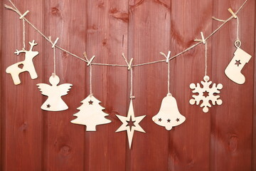 A rope garland of Christmas and New Year decorations made of plywood on a red wooden background.	