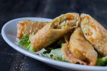 Homemade spring rolls on a bed of lettuce. In a white plate on a wooden background