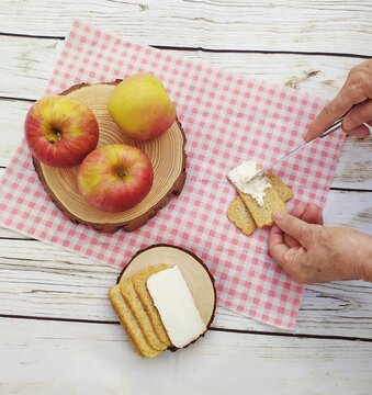 Overhead view of a person spreading cream cheese on a cracker with fresh apples