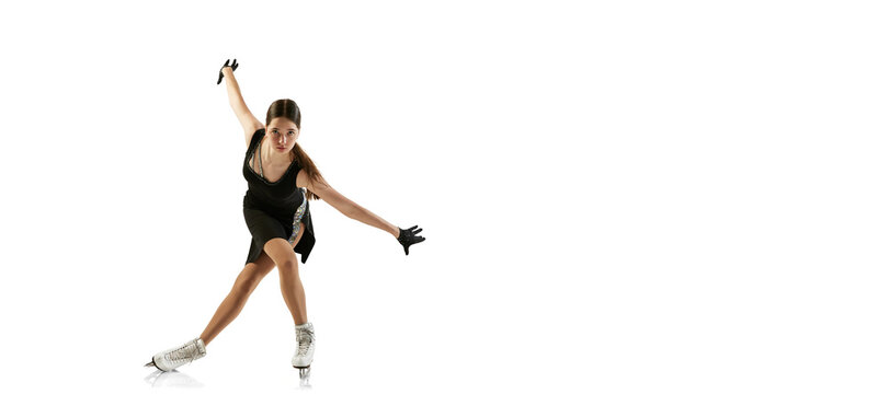 Portrait of flexible young girl, female figure skater in black stage costume skating isolated over white background. Junior athlete in motion. Sport, beauty, winter sports