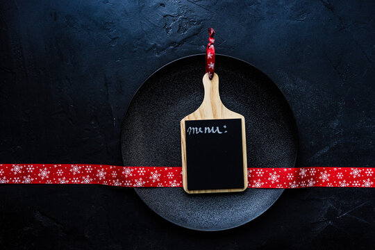 Overhead view of a blank individual menu blackboard on a plate with a festive Christmas ribbon
