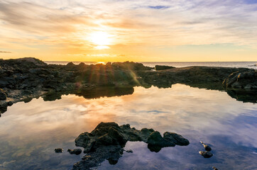 Fototapeta na wymiar beautiful sea sunrise on a rocky sea coast with calm water , amazing cloudy sky and reflection on water surface