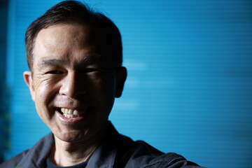 A craftsman poses in gray work clothes in front of blue shutter of a factory. Conceptual images of the essence of manufacturing, technical succession and the challenge of high-precision machining.