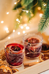 Cozy close-up of two glasswes with mulled wine. Christmas drink. Xmas tree and garland lights. Winter beverage
