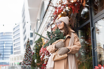 Stylish young woman with branches of nobilis walks through the Christmas city