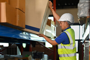 Man warehouse worker wearing hard hats and reflective jackets taking package on the shelf of warehouse
