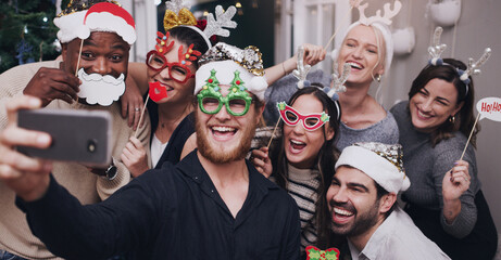 Christmas, party and friends taking a selfie on a phone together with goofy, funny and silly props. Diversity, festive and happy people taking picture on a smartphone at festive xmas event at a home. - obrazy, fototapety, plakaty