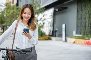 Portrait of beautiful smile business woman commute her bicycle outdoor using smartphone at urban, bike go to work office, Asian businesswoman standing on city street with bicycle holding mobile phone