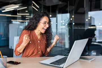 Hispanic business woman celebrating victory success, employee with curly hair inside office reading...
