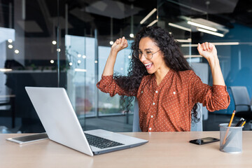 Hispanic business woman celebrating victory success, employee with curly hair inside office reading...