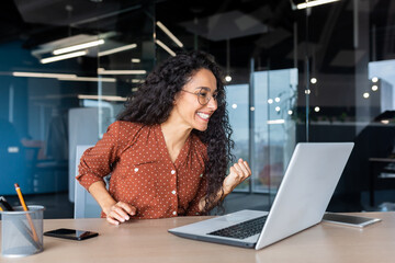 Hispanic business woman celebrating victory success, employee with curly hair inside office reading...
