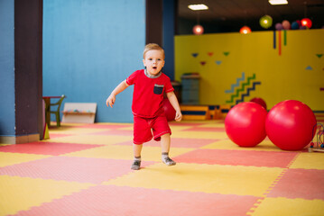 Happy laughing boy 1-2 years old playwith large balls in kids amusement park and indoor play center. Child playing with colorful balls in playground ball pool. Activity toys for little kid