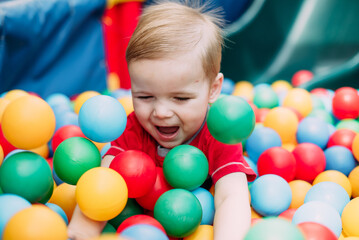 Happy laughing boy 1-2 years old having fun in ball pit  in kids amusement park and indoor play center. Activity toys for little kid