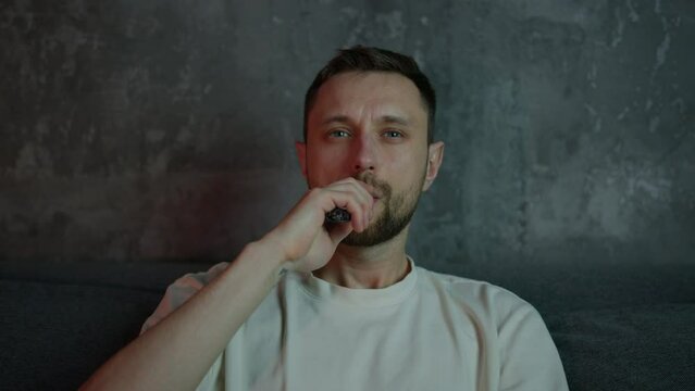 Close-up of a hipster man smoking an electronic cigarette sitting at home in front of the TV