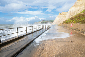 Obraz premium Big waves and water splashes at West Bay beach near Bridgport in Dorset, United Kingdom. Walkway or promenade along the beach, selective focus