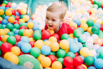 Obraz na płótnie Canvas Happy laughing boy 1-2 years old having fun in ball pit in kids amusement park and indoor play center. Activity toys for little kid