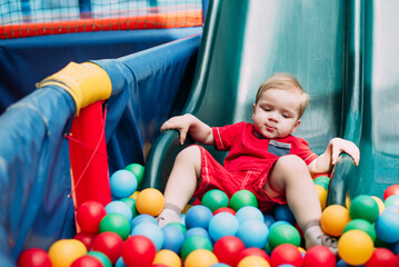 Happy laughing boy 1-2 years old having fun in ball pit  in kids amusement park and indoor play center. Activity toys for little kid