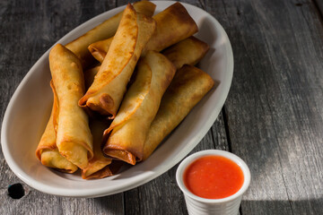 Homemade spring rolls with chinese sweet and sour sauce. In a white plate on a wooden background