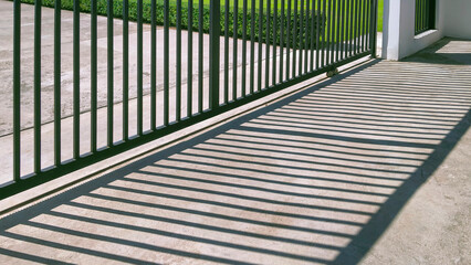 Sunlight and shadow on surface of automatic sliding metal fence gate in front of modern house,...