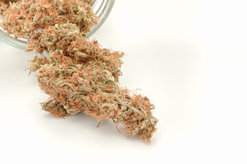 Dry marijuana buds outside of a jar on a white background