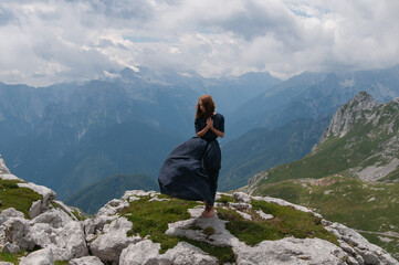 Beautiful young woman posing in a high mountain landscape. Rocky mountain. A young woman in a long dress stands on the edge of a cliff