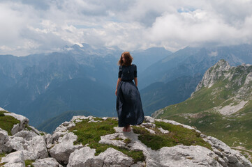 Beautiful young woman posing in a high mountain landscape. Rocky mountain. A young woman in a long dress stands on the edge of a cliff

