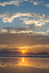 Incredible seascape. Sunset on the beach, clouds golden in the sun. the sun sets behind the mountains. silhouettes of mountains. The ocean washes the sand on the beach. Golden clouds. Background. Lanz