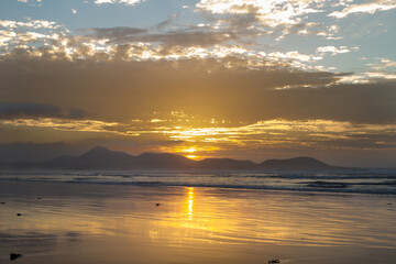 Obraz premium Incredible seascape. Sunset on the beach, clouds golden in the sun. the sun sets behind the mountains. silhouettes of mountains. The ocean washes the sand on the beach. Golden clouds. Background. Lanz