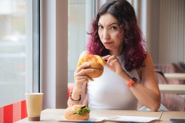 Frowned disgruntled girl customer of a fast food restaurant digs into a burger and found a spoiled...