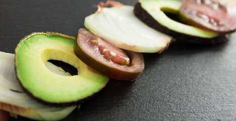 chopped vegetables black tomatoes, avocado and onions against black stone board