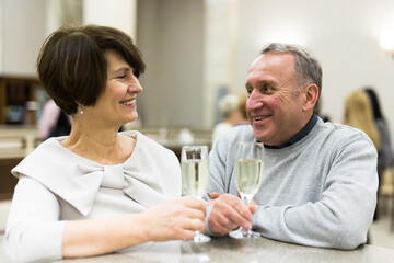 Caucasian couple senor and senora drink champagne in the lobby of theater during intermission