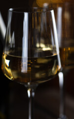 Two glasses of white wine and a bottle on a wooden table and lights garlands behind