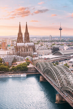 Cologne Aerial vertical view with trains move on a bridge over the Rhine River on which cargo barges and passenger ships ply. Majestic Cologne Cathedral in the background