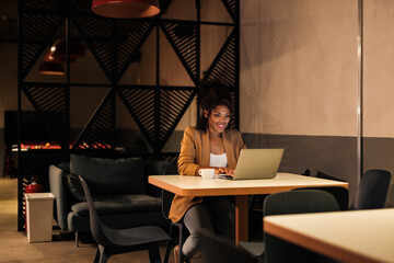 Smiling African woman enjoying working late at night, sitting at the office.