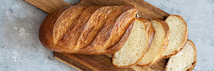 Freshly baked loaf on a wooden board on a light gray (blue) background. Traditional fresh bread in...