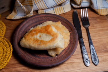 Clay plate of fried meat pies with cutlery on wooden table.